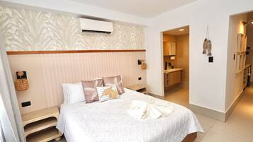 Habitación de hotel ordenada con cama, mesitas de noche, unidad de aire acondicionado, espejo y baño visible a través de una puerta abierta.