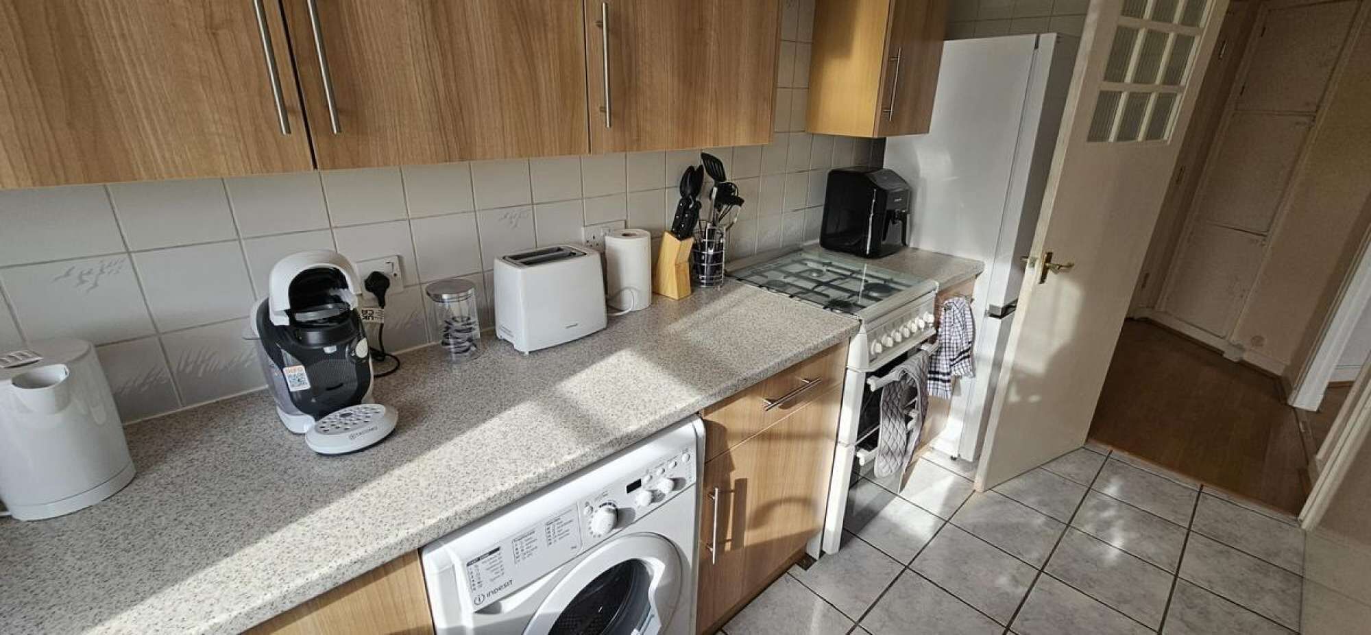Eine kleine Küche mit Waschmaschine, Kaffeemaschine, Toaster und Herd.