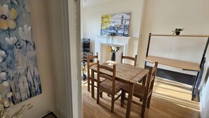 A dining area with a wooden table and chairs, a painting on the wall, and a view of a cityscape through a window.