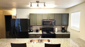 A kitchen with granite countertops, a sink, a stove, a microwave, and green cabinets.