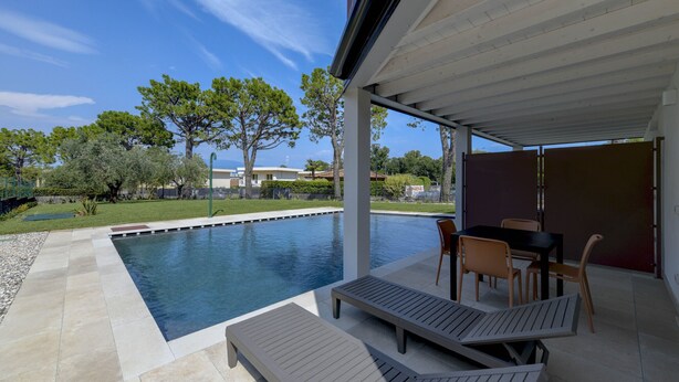 A swimming pool with lounge chairs and a table, surrounded by a covered patio area. - Gardaliva 7 by the lake in Manerba (Manerba del Garda)