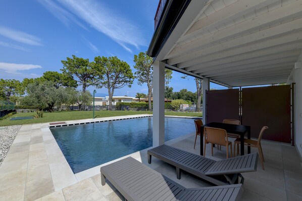 Ein Swimmingpool mit Liegestühlen und einem Tisch, umgeben von einer überdachten Terrasse.
