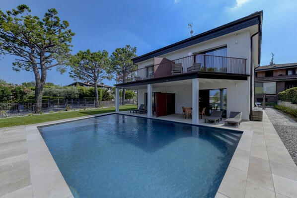 A modern two-story house with a swimming pool, outdoor seating, and a fenced garden.