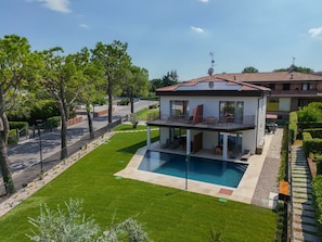 A modern two-story house with a swimming pool, surrounded by a well-maintained lawn and trees.