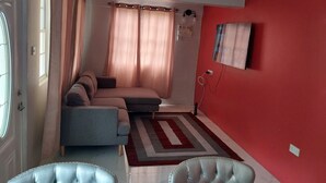 Ein Wohnzimmer mit einer Couch, einem Teppich, einer roten Wand und einem Fenster mit Vorhängen.