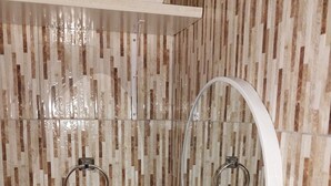 Ein Badezimmer mit Waschbecken, Spiegel und Handtuchhaltern an einer gefliesten Wand.