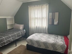 A bedroom with two beds, a window with curtains, a wall-mounted shelf, and a painting. - Contemporary Cottage 5 min walk to major bike path (Lincoln)