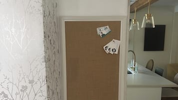 A room with a corkboard on the wall, a wooden ceiling, and a dining area with chairs and a table.