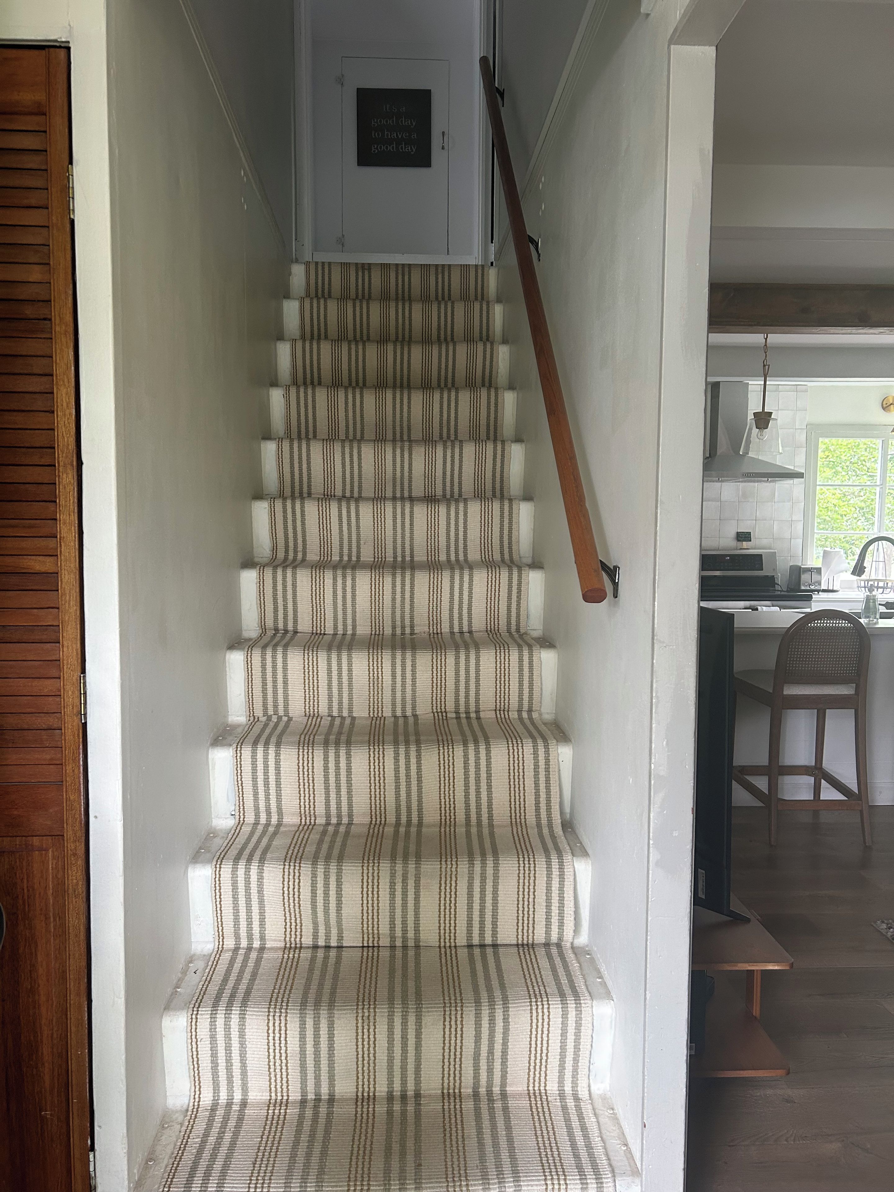 A staircase with striped carpet leading to a door with a plaque.
