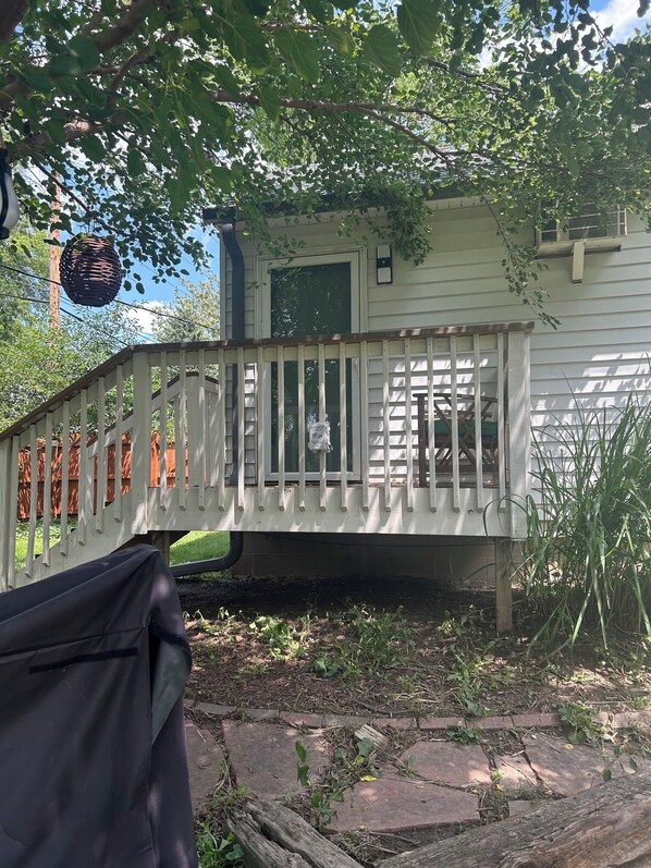 Un espace extérieur abrité doté d’une terrasse en bois, d’un petit bâtiment avec une porte et d’un pot suspendu.