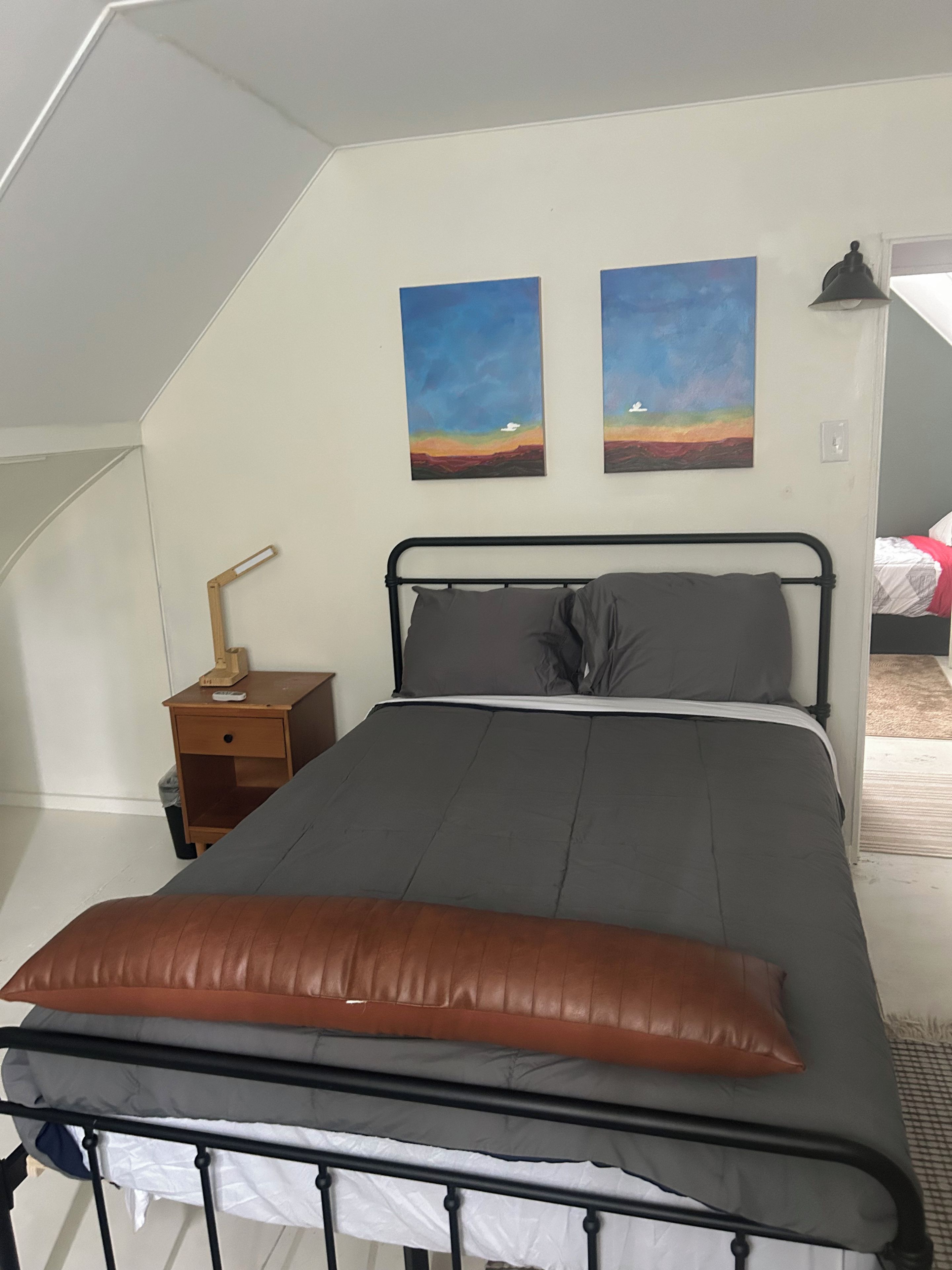 A bedroom with a bed, a nightstand, two paintings, and a lamp.