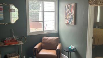 A room with a brown leather chair, a window, a small table, and a cabinet with board games.