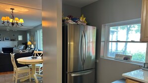 Una cocina moderna con un refrigerador de acero inoxidable, un comedor con una mesa redonda y sillas, y un ventanal con vistas a árboles.