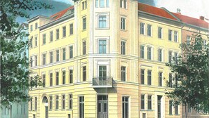 A multi-story building with a corner entrance, large windows, and a balcony with ornate railings.