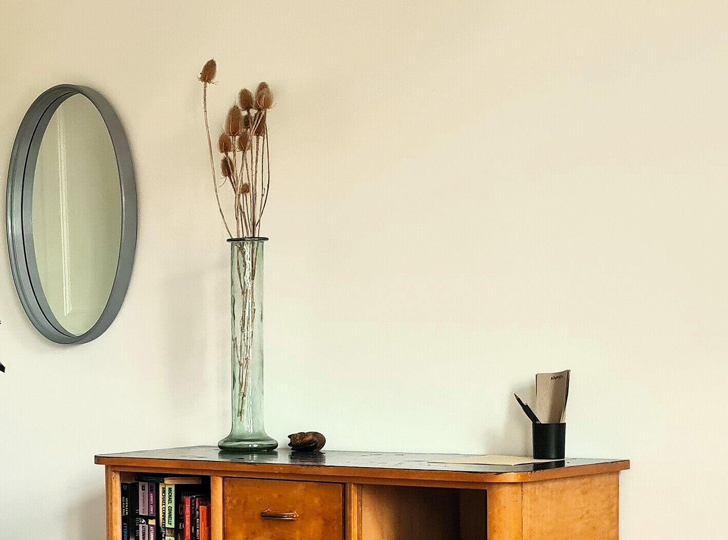 A room with a wooden cabinet, a mirror, and a vase with dried plants.