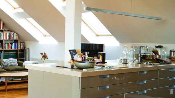 A modern kitchen with a skylight, a dining area with a sofa, and a bookshelf.