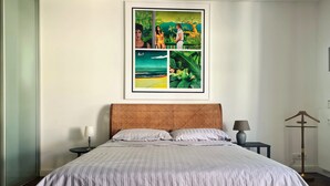 A bedroom with a large bed, a framed picture above it, a nightstand with a lamp, and a coat rack.