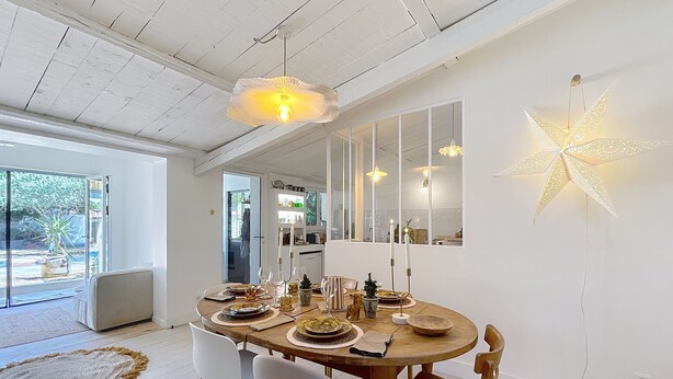 A dining area with a round wooden table set for four, surrounded by white chairs. There are candles on the table, and a star-shaped light fixture hangs above. - House N8 Arles - 5mns from the center, seasonal rental in a relaxing setting! (Arles)