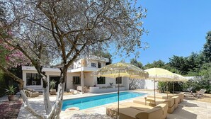 A modern outdoor pool area with lounge seating and umbrellas, surrounded by a landscaped garden and a white building with large windows. - House N8 Arles - 5mns from the center, seasonal rental in a relaxing setting! (Arles)