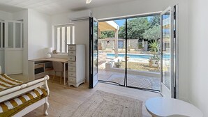 A bedroom with a bed, a desk, and a view of an outdoor swimming pool. - House N8 Arles - 5mns from the center, seasonal rental in a relaxing setting! (Arles)