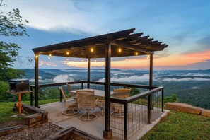 Un mirador con luces colgantes, asientos al aire libre y vistas de un paisaje montañoso.