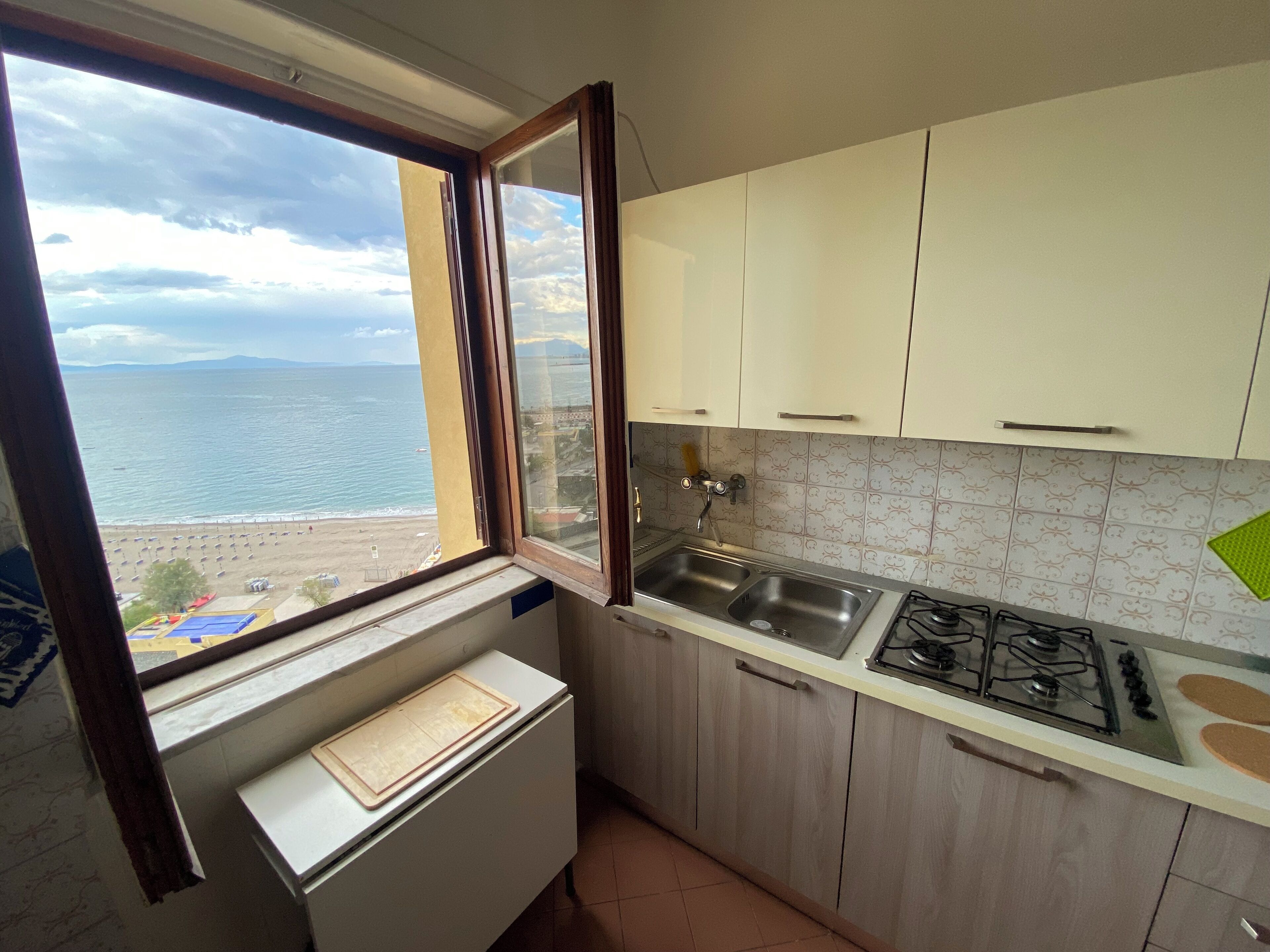 A kitchen with a window view of the sea, a sink, and a stove.