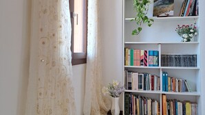 A room with a large window, a bookshelf filled with books, a potted plant, and a decorative curtain.