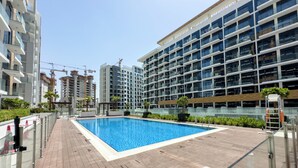 A modern building with a swimming pool, glass railings, and a paved walkway.