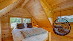 A cozy wooden cabin bedroom with a bed, pillows, and a hanging chair.