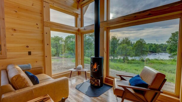 A cozy cabin interior with a large window, a fireplace, and a wooden floor.