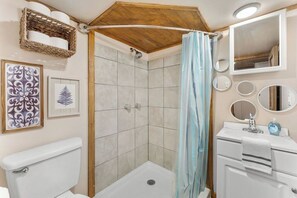 Un baño con ducha, inodoro, lavamanos y varias fotografías enmarcadas en la pared.
