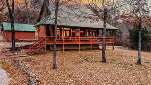 Una baita di legno con un portico e una scala, immersa tra alberi e un cielo sereno.