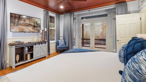 Una camera da letto con un letto grande, un ventilatore a soffitto, una TV, un comodino e vista sull'esterno attraverso una porta.