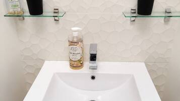 Une salle de bain avec un lavabo blanc, un miroir au-dessus, et deux étagères en verre où sont rangés les articles de toilette.