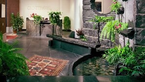 A lobby with a reception desk, a stone wall with a circular cutout, a small water feature, and various potted plants.