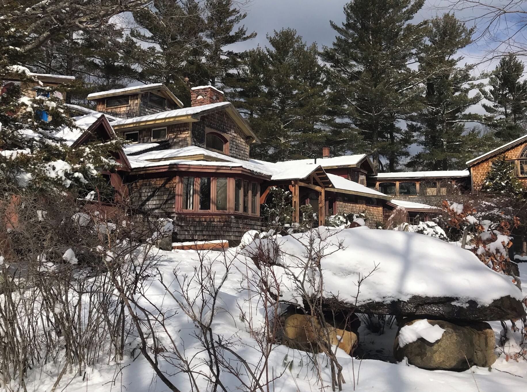 Una cabaña nevada con varios edificios, rodeada de árboles y rocas.
