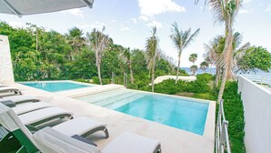 A pool area with lounge chairs and a view of the sea.