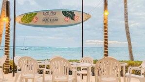 A beachside snack bar with a view of the ocean, surrounded by white plastic chairs and palm trees. - Nido De Tortuga 2 Min Beach Access Private Jacuzzi (Akumal)