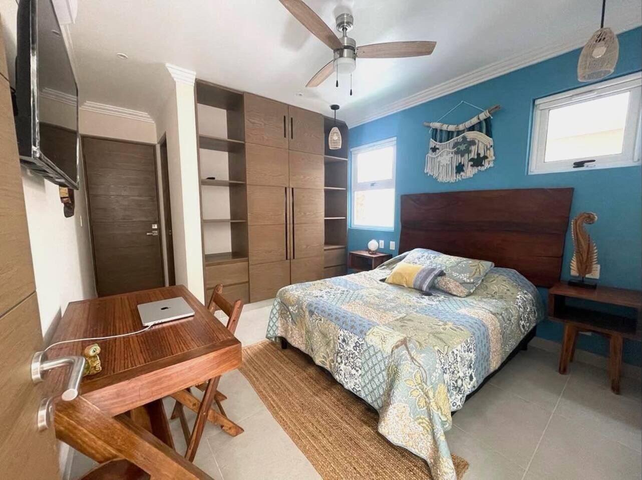 A bedroom with a bed, a desk, a chair, a ceiling fan, and built-in shelving.