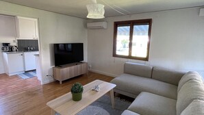 Ein Wohnzimmer mit einer Couch, einem Couchtisch und einem Fernseher. Es gibt eine Küchenzeile mit Schränken und einer Mikrowelle.
