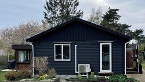 Ein dunkelblaues Einfamilienhaus mit Veranda, ein kleiner Garten mit Narzissen und ein großer Baum im Hintergrund.