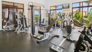 A modern gym with various exercise equipment, large windows offering views of greenery and buildings, and a clean, well-lit interior. - NEW 2BR/2BA w/Private Jacuzzi minutes from beaches. Gym/Pools/Tennis/Restaurant (Noord)