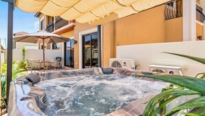 A hot tub with a beige umbrella, a table with chairs, and a building with balconies. - NEW 2BR/2BA w/Private Jacuzzi minutes from beaches. Gym/Pools/Tennis/Restaurant (Noord)