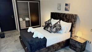 Una cama bien tendida con sábanas blancas y almohadas estampadas en blanco y negro, una mesita de noche con lámpara y un armario con espejo.