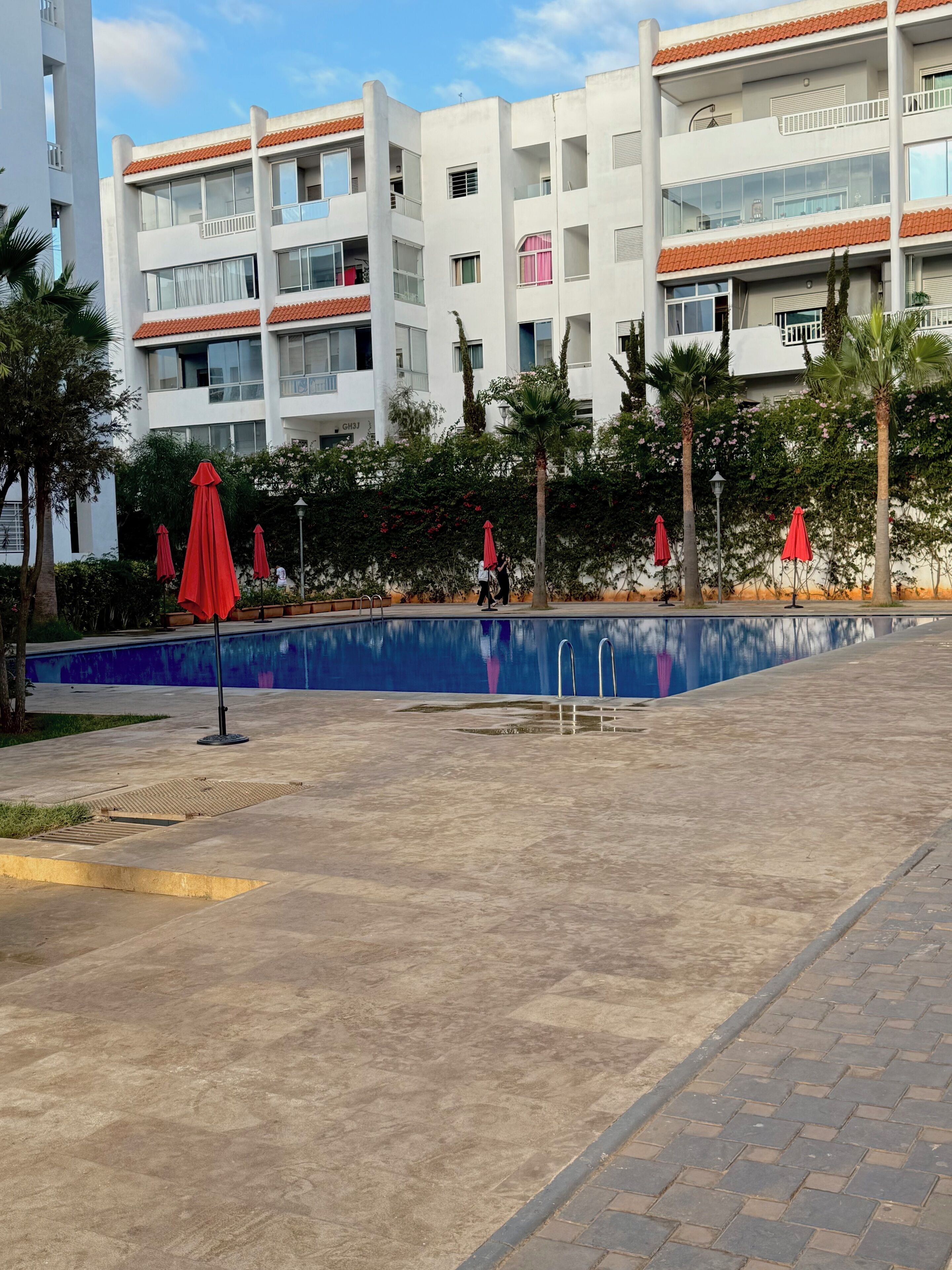A modern building with balconies, a swimming pool, and red umbrellas.