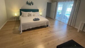 Une chambre spacieuse avec un grand lit, une tête de lit de couleur turquoise et une vue sur une piscine, visible à travers la porte vitrée.