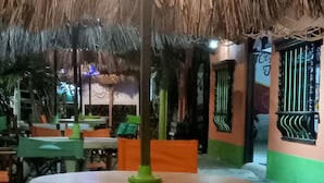 Un espacio de estar al aire libre cubierto, con una mesa central y sillas, rodeado por una estructura de techo de paja.
