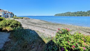 A coastal view with a beach, a row of houses, and a forested island in the distance. - Heron's Nest is a waterfront spectacular 3-bedroom townhome in Port Ludlow (Port Ludlow)