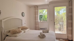 Ein Schlafzimmer mit Bett, Kissen, Nachttisch, Fenster und Blick ins Grüne.