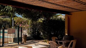 Ein Außenbereich mit einer Strohgedeckten Terrasse, weißen Plastikstühlen und einem Fliesenboden.